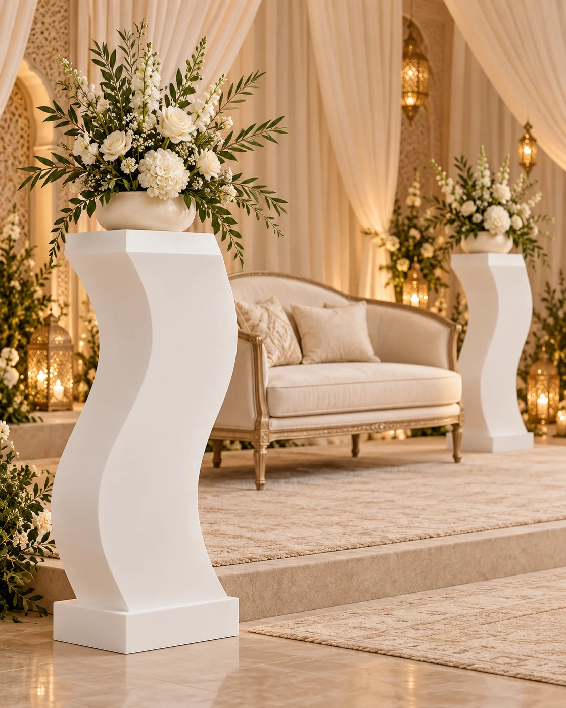 Présentoirs sculpturaux blancs avec compositions florales sur une estrade de mariés